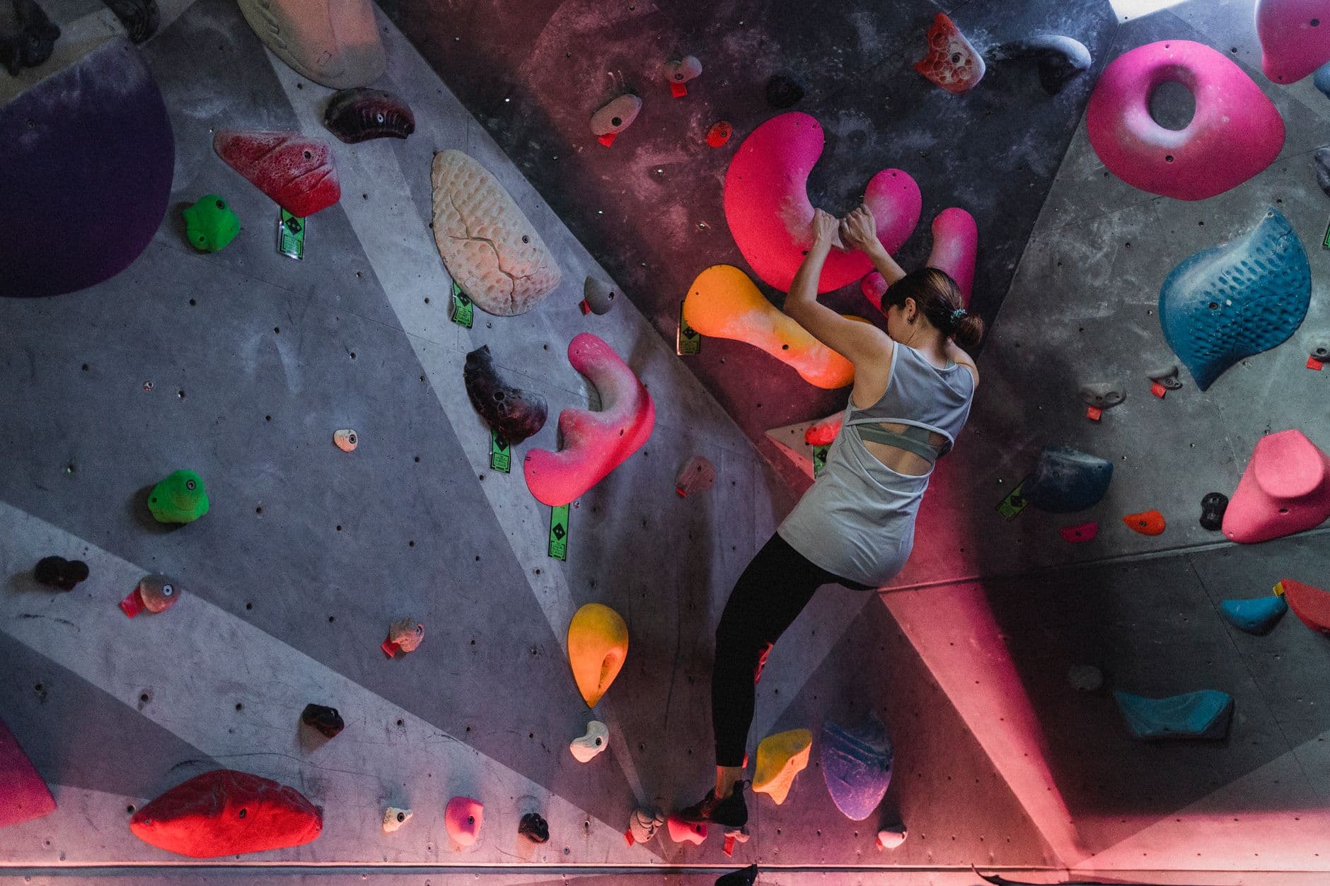 A climber high on an indoor wall reaching for a hold