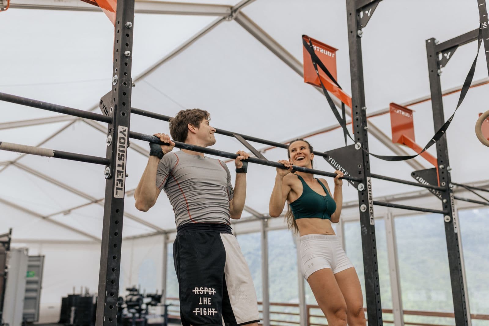 Two people hanging from a pull-up bar in an indoor gym