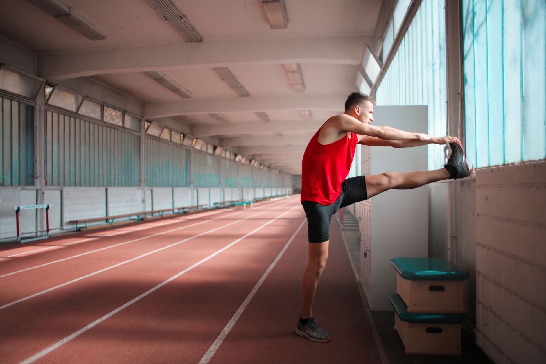 A runner stretching at the side of an indoor track