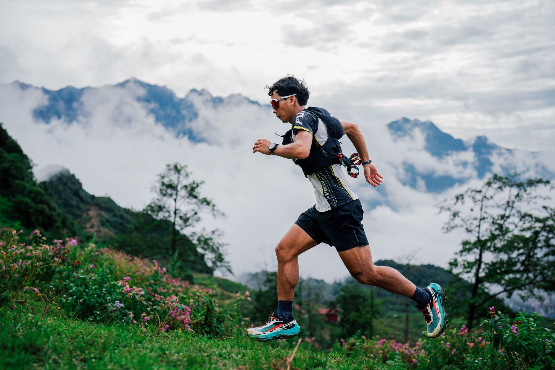 A trail runner on a mountain path with peaks and cloud behind