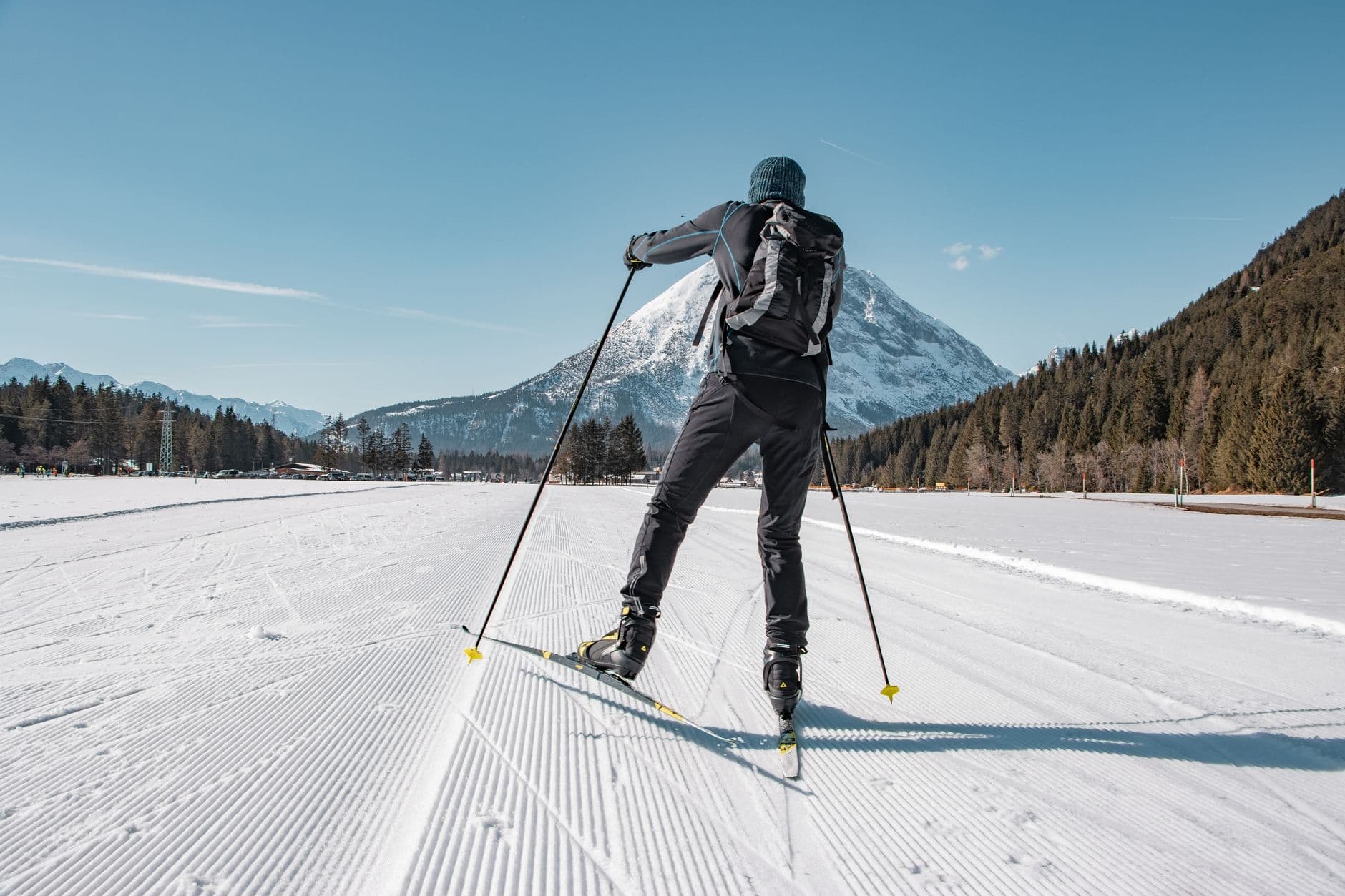 A cross-country skier on a groomed track below a snowy peak